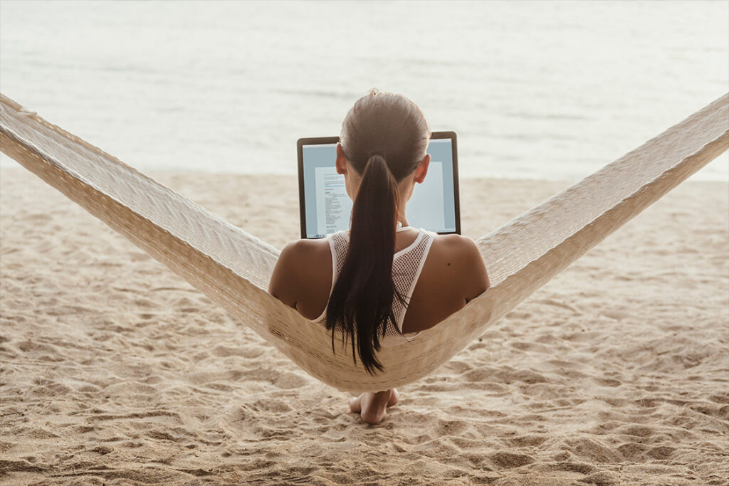 Laptop user sitting in hammock on the beach