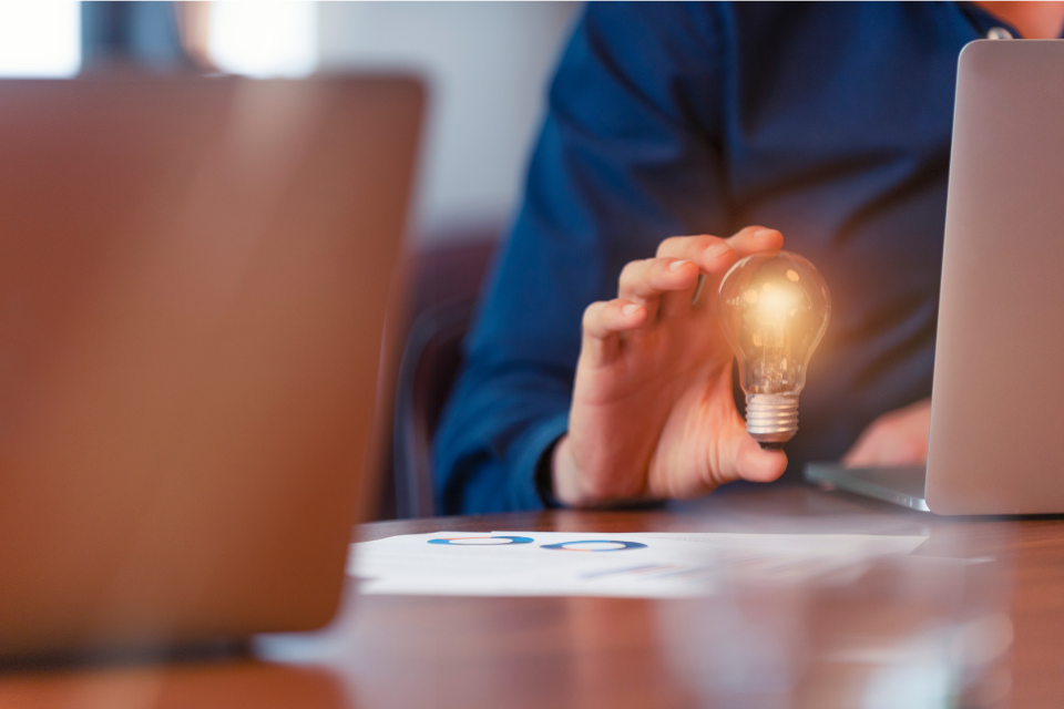 A worker sitting in front of a laptop and holding a lightbulb in his right hand